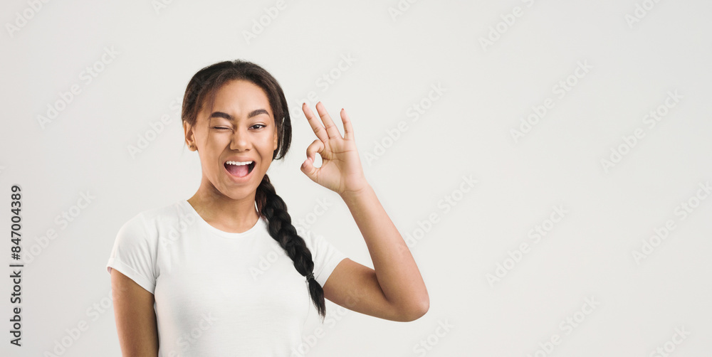 A young Black girl is depicted making the OK gesture with her hand. She has a neutral expression on her face and appears to be gesturing in a casual manner. A young Black girl is depicted making the OK gesture with her hand. She has a neutral expression on her face and appears to be gesturing in a casual manner.