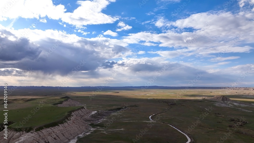 Fototapeta premium Vast prairie desert landscape in Badlands South Dakota with sunshine, farmland, clouds and blue sky dramatic view in nature's hot climate