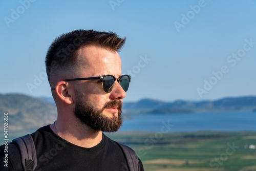 A handsome young Albanian man wearing sunglasses looking at a landscape of Albanian riviera in southern Albania. 