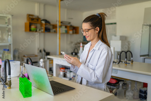 Smiling female scientist using smartphone while working in lab photo