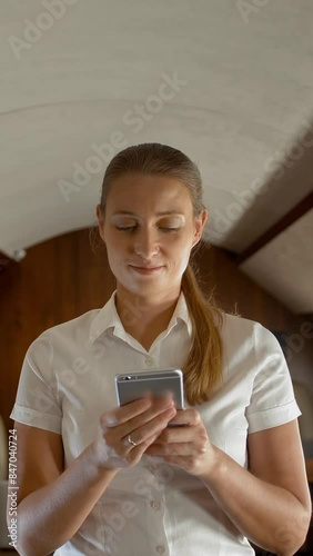 Portrait of busy young woman typing messages in smartphone in private jet. Deal working female with cell phone in airplane chatting on selphone staying in the cabin. 4k UHD Vertical shot. photo