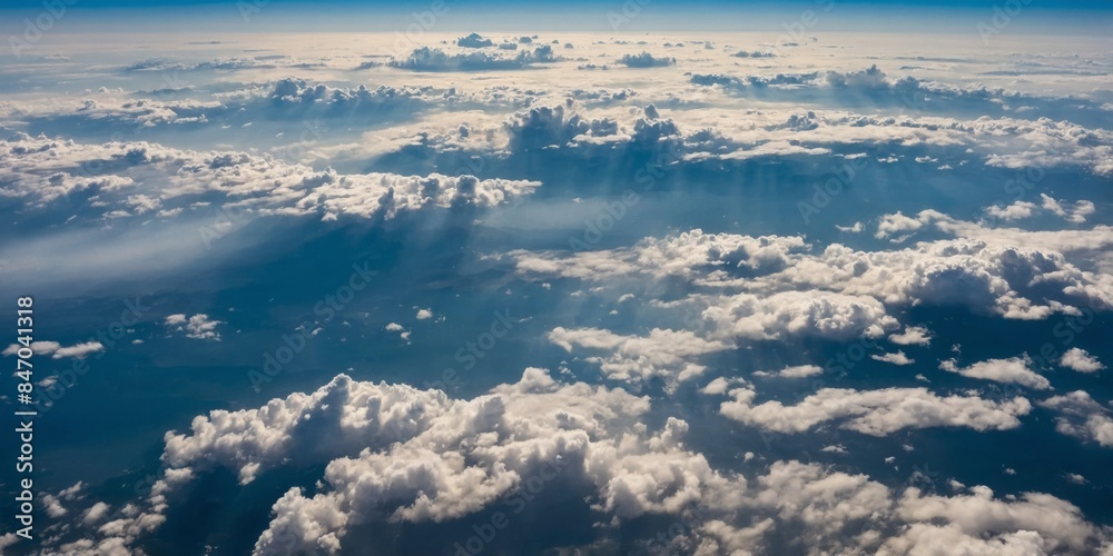 An aerial view from an airplane shows a vast cloudscape with sunrays piercing through clouds An aerial view from an airplane shows a vast cloudscape with sunrays piercing through clouds