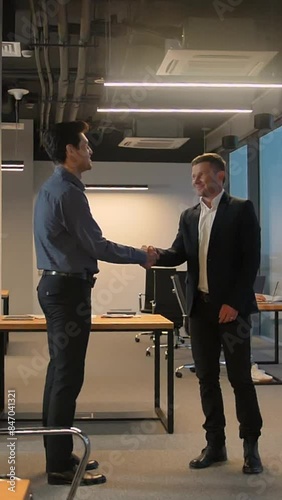 Two businesspeople shaking hands inside of modern business office. Deal friendly relationship, super slow motion shot. Vertical shot.