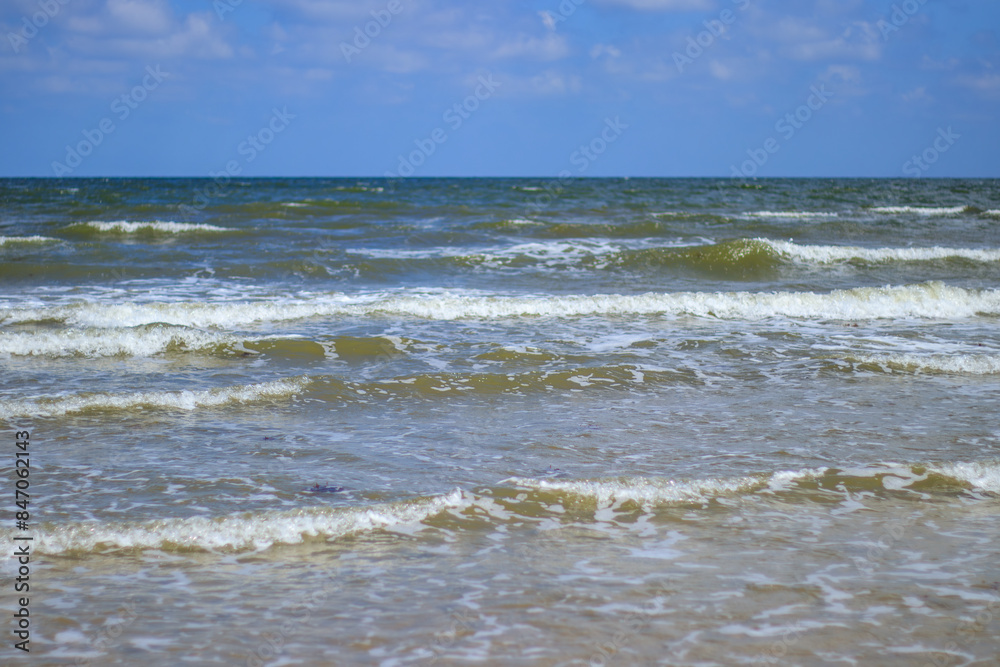 Discover the beauty of Galveston Island, Texas, where gentle waves caress the sandy shore beneath a picturesque cloudy sky. The lively sea, adorned with frothy whitecaps, for beach lovers.