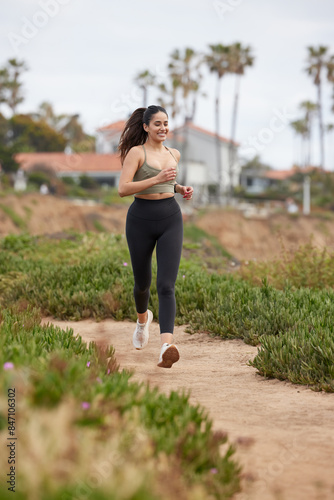 Hispanic female runner running towards camera, wearing dark tights and olive top.