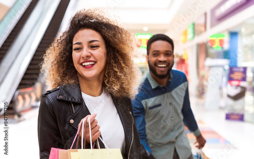 African American man and woman are walking down a busy shopping mall carrying multiple shopping bags. The man is carrying a few bags while the woman is holding more. photo
