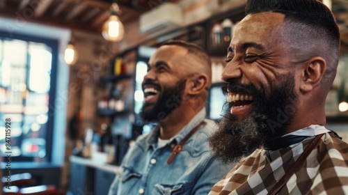 Two men with beards laugh together in a barbershop. © Prostock-studio