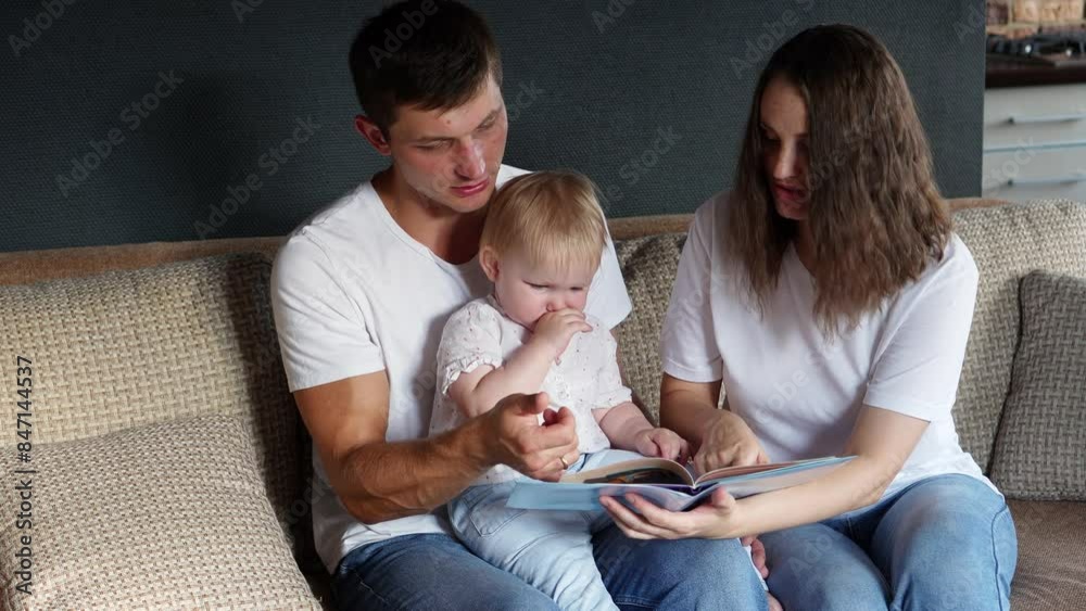 Man and woman sit on sofa and read book to baby, sharing moments of comfort and relaxation. Concept of family vacation together, learning, education. Man and woman sit on sofa and read book to baby, sharing moments of comfort and relaxation. Concept of family vacation together, learning, education.