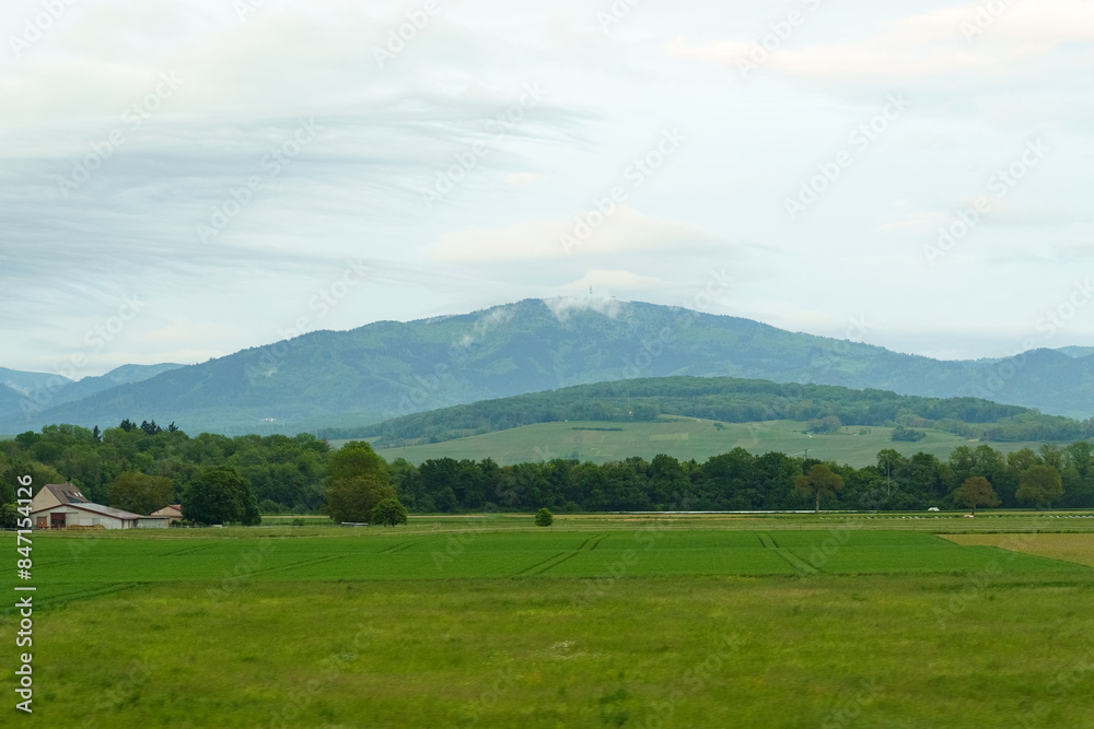 Fototapeta premium A Farmhouse in Front of Rolling Hills and Cloudy Mountains