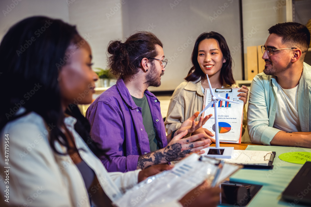 A group of four young people from diverse backgrounds gather around a model wind turbine. They share their thoughts and ideas about sustainable energy sources. A group of four young people from diverse backgrounds gather around a model wind turbine. They share their thoughts and ideas about sustainable energy sources.
