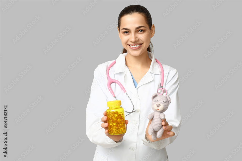 Portrait of female doctor with pills and toy on grey background Portrait of female doctor with pills and toy on grey background