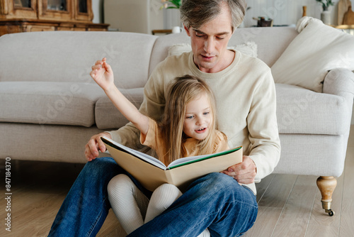 Father reading to daughter near couch photo