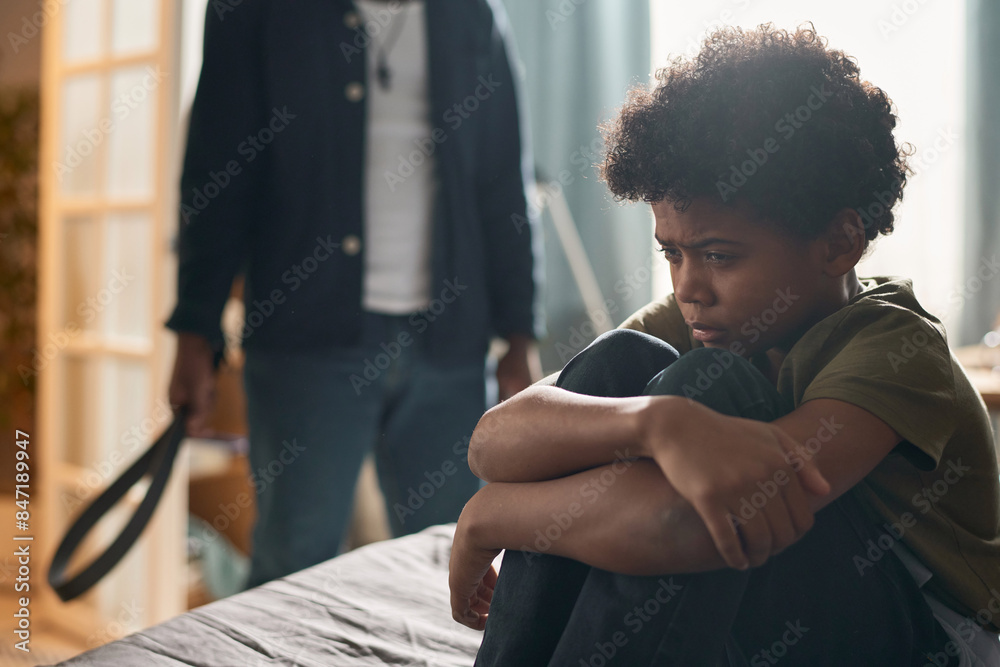 Side view portrait of Black little boy crying sitting on bed in dark