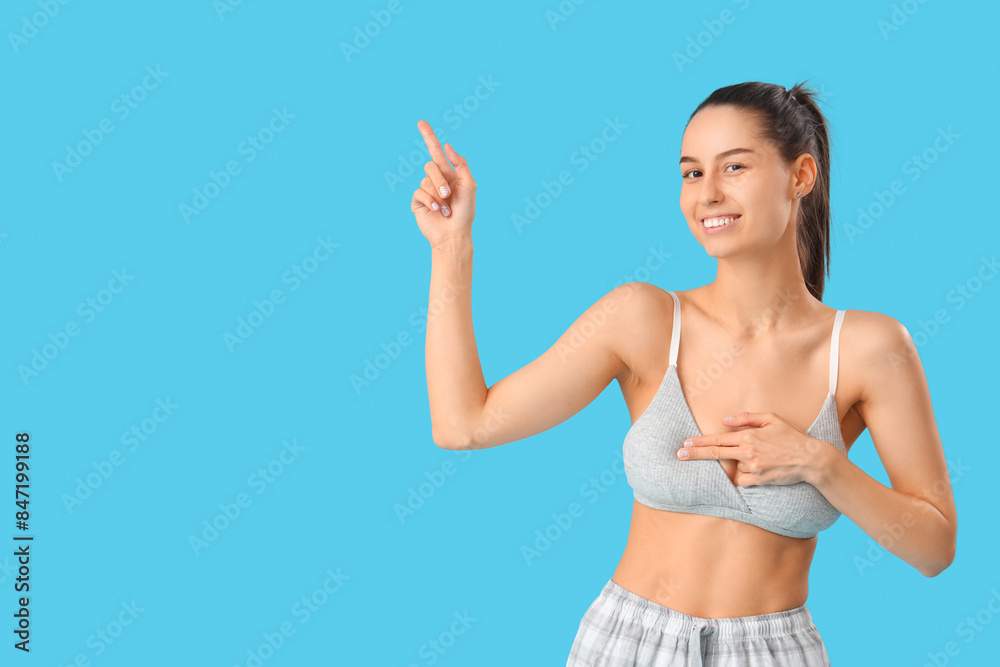 Young woman pointing at something on blue background. Breast cancer awareness concept