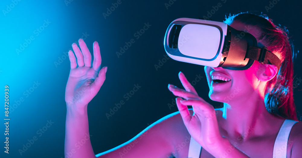 A woman is wearing a virtual reality headset, fully engrossed in a digital world. The headset covers her eyes and ears, while she explores a simulated environment through hand gestures
