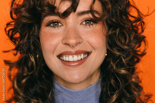 Joyful young woman with curly hair on orange background