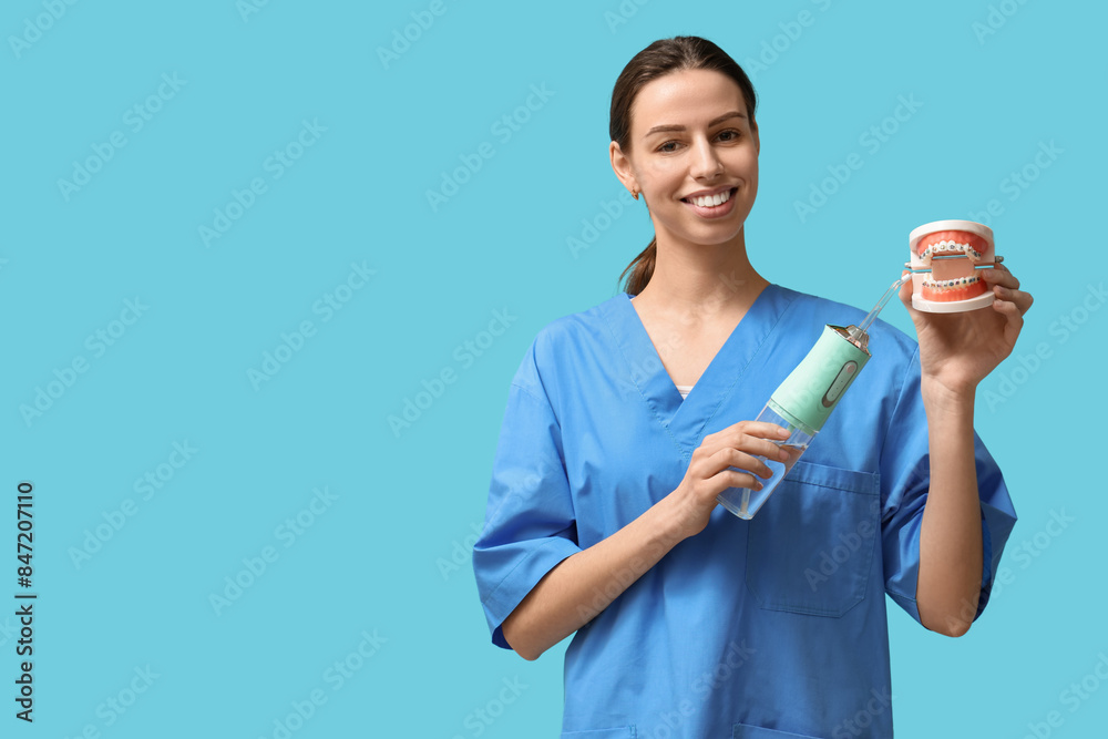 Female dentist with oral irrigator and jaw model on blue background Female dentist with oral irrigator and jaw model on blue background