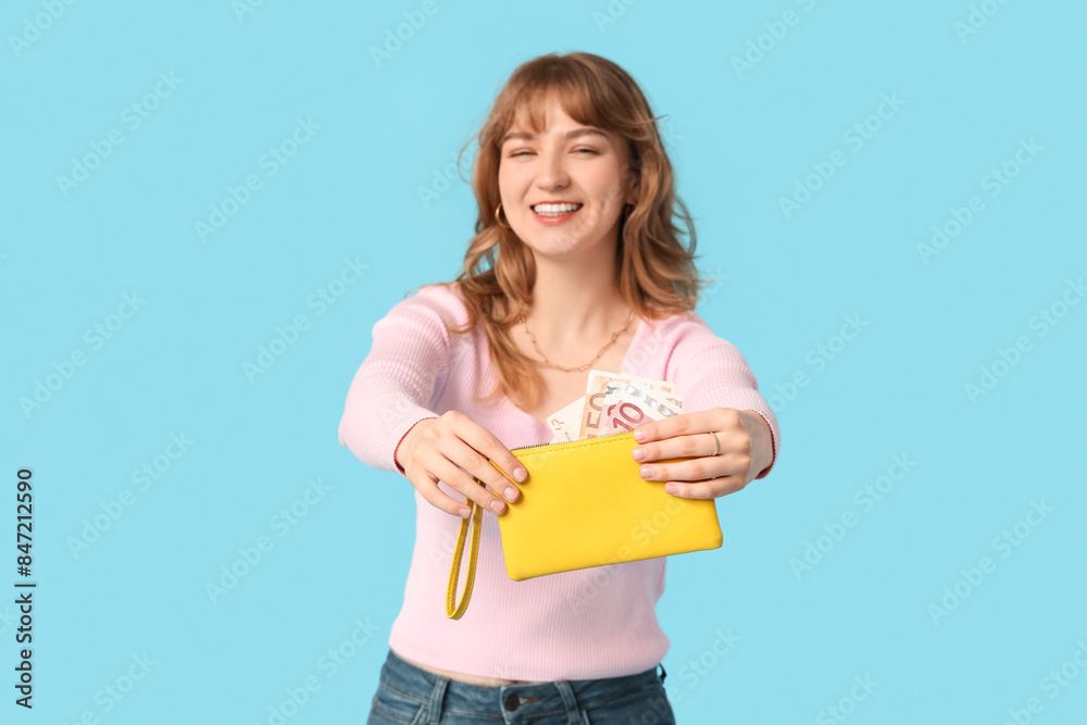 Beautiful young woman holding yellow wallet with money on blue background Beautiful young woman holding yellow wallet with money on blue background