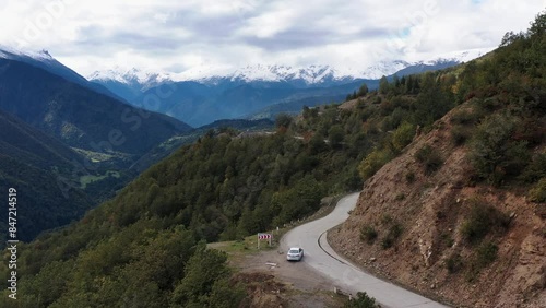 Aerial view of the road among the mountains. The car drives among beautiful and high mountains. All around are mountainous expanses, trees, nature. 4k drone video.