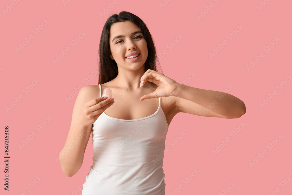 Happy smiling young woman holding crystal deodorant and making heart with her hand on pink background Happy smiling young woman holding crystal deodorant and making heart with her hand on pink background