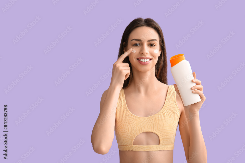 Beautiful young woman applying sunscreen cream on her face against lilac background Beautiful young woman applying sunscreen cream on her face against lilac background