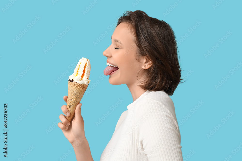 Beautiful young woman with sweet ice-cream in waffle cone showing tongue on blue background Beautiful young woman with sweet ice-cream in waffle cone showing tongue on blue background