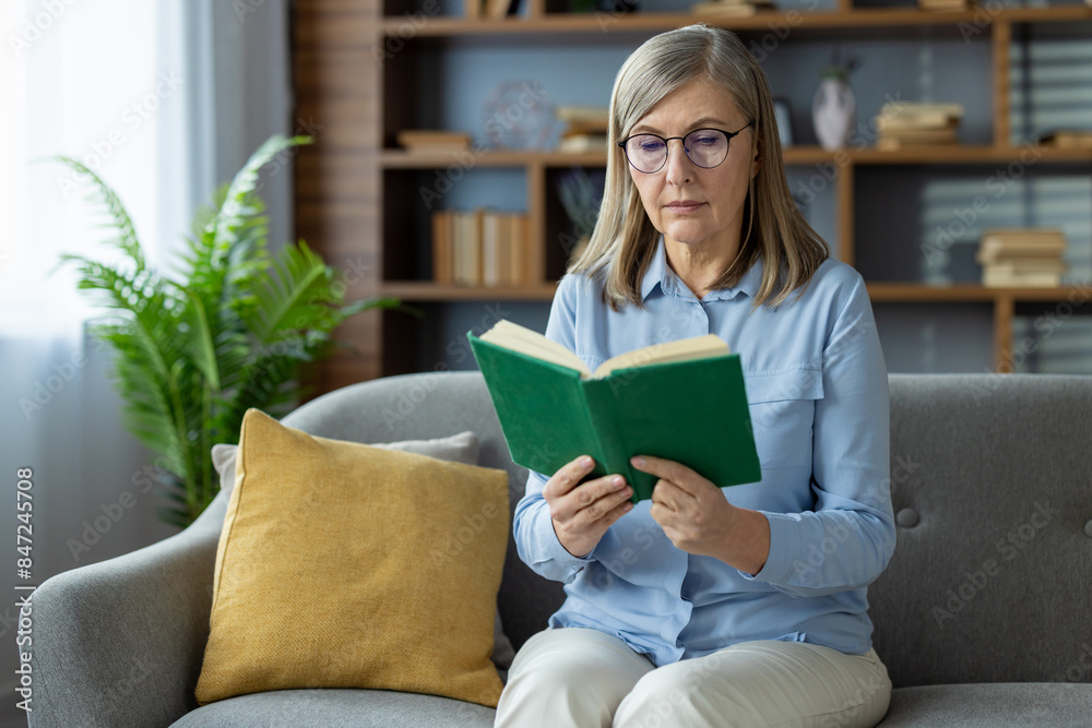 Middle-aged woman enjoying a book while sitting on a cozy sofa at home, conveying relaxation and leisure time. Middle-aged woman enjoying a book while sitting on a cozy sofa at home, conveying relaxation and leisure time.