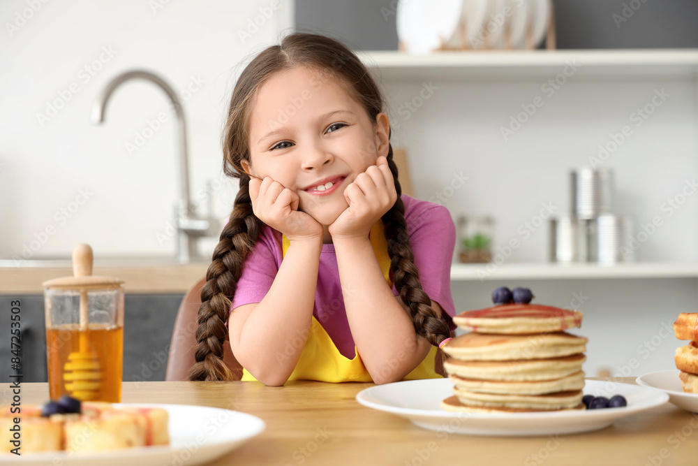 Cute little girl and pancakes with honey on table in kitchen Cute little girl and pancakes with honey on table in kitchen