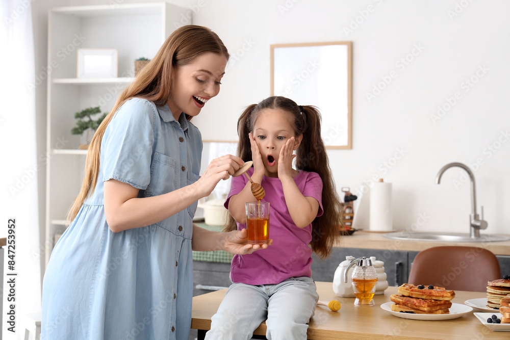 Surprised little girl and her mother with honey in kitchen Surprised little girl and her mother with honey in kitchen