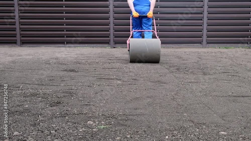 male worker in a uniform prepares a plot of land for sowing a lawn using a lawn roller, leveling and compacting the earth	