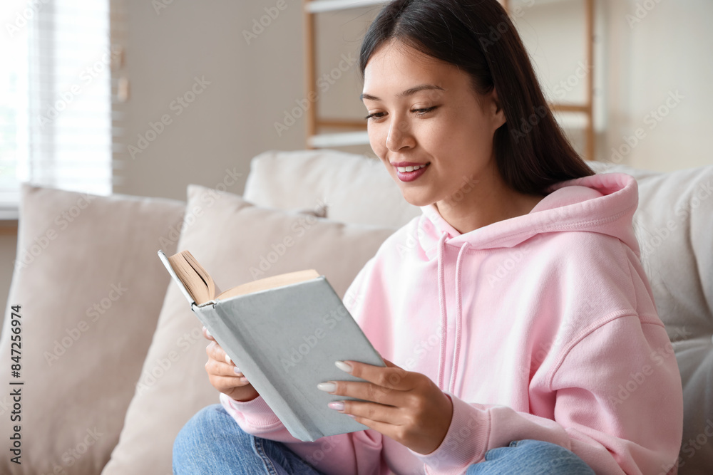 Beautiful young woman reading book and sitting on couch at home Beautiful young woman reading book and sitting on couch at home
