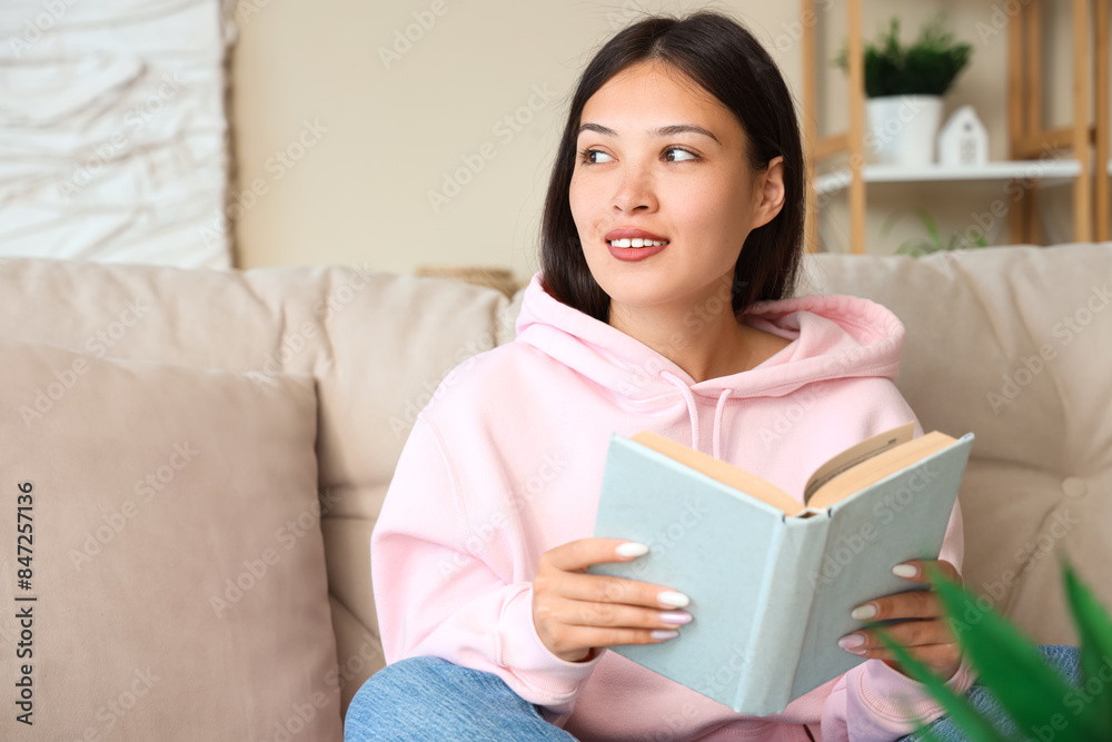 Beautiful young woman reading book and sitting on couch at home Beautiful young woman reading book and sitting on couch at home