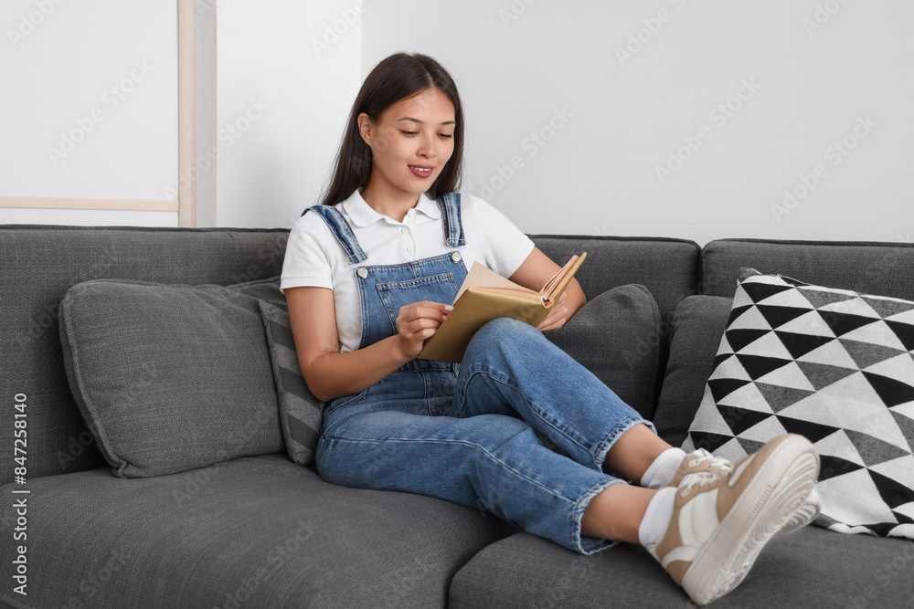 Beautiful young woman reading book and sitting on black sofa at home Beautiful young woman reading book and sitting on black sofa at home