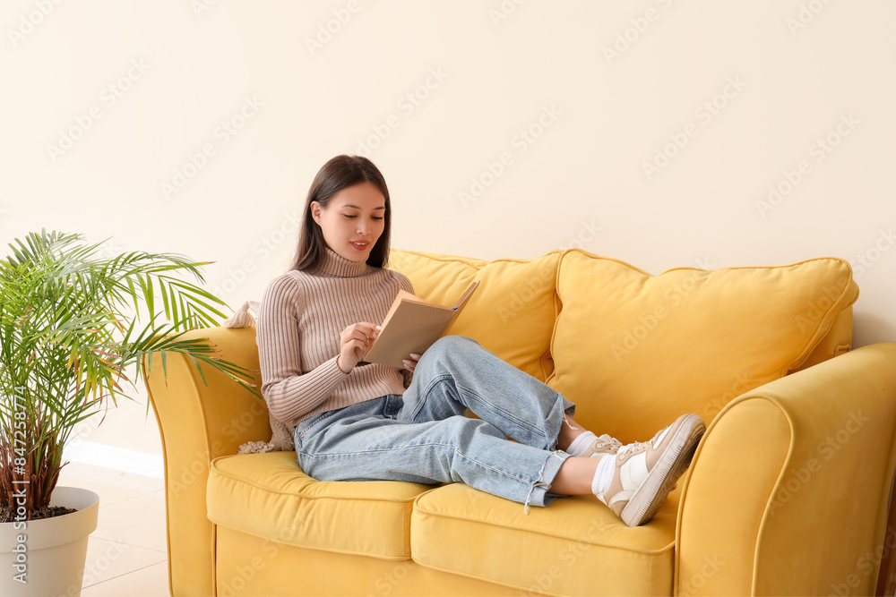 Beautiful young woman reading book and sitting on yellow sofa at home Beautiful young woman reading book and sitting on yellow sofa at home