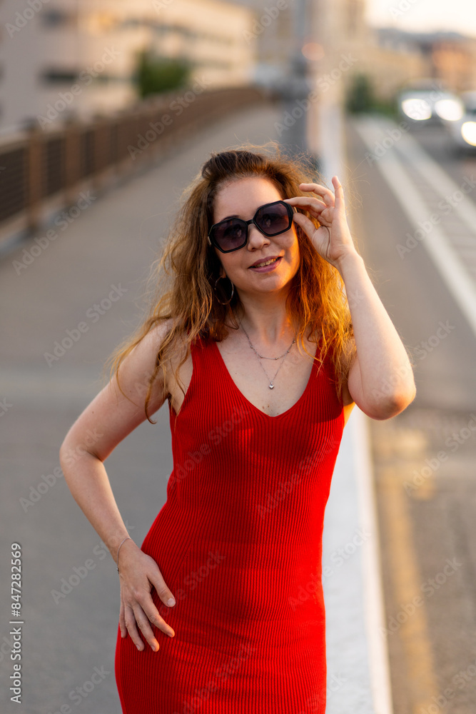 Cute young beautiful attractive woman with long hair in a red dress. Cityscape, urban summer walks, sunset bright sunlight. Happiness, confidence, freedom Cute young beautiful attractive woman with long hair in a red dress. Cityscape, urban summer walks, sunset bright sunlight. Happiness, confidence, freedom