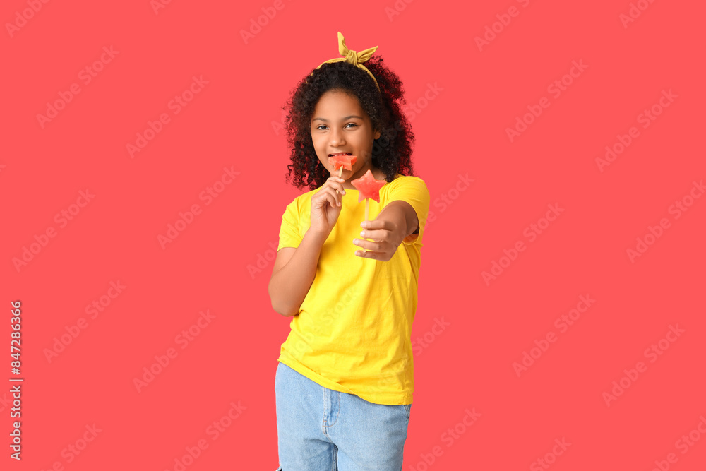 Cute African-American girl holding sticks with sweet watermelon in shape of stars on red background Cute African-American girl holding sticks with sweet watermelon in shape of stars on red background