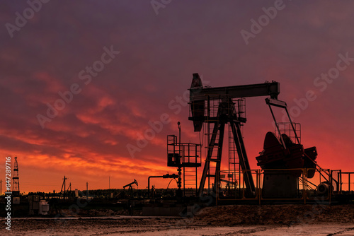 Oil drill rig silhouette and pump jack at sunset background.