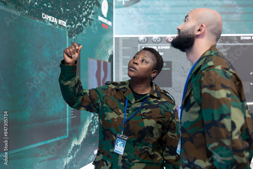 Male and female engineers talking about a new operation next to a big screen, examining real time satellite surveillance data. Military IT operators work on telecommunications. photo