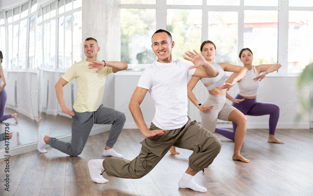 Fototapeta premium Emotional sporty young Asian dancer rehearsing modern krump dance moves during group workout in studio