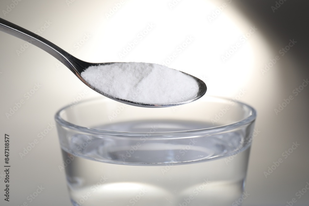 Spoon with baking soda over glass of water on light background, closeup Spoon with baking soda over glass of water on light background, closeup