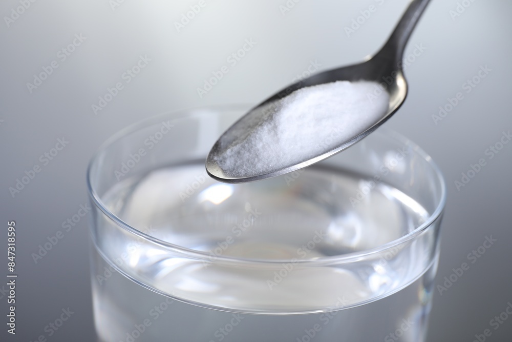 Adding baking soda into glass of water on light grey background, closeup Adding baking soda into glass of water on light grey background, closeup