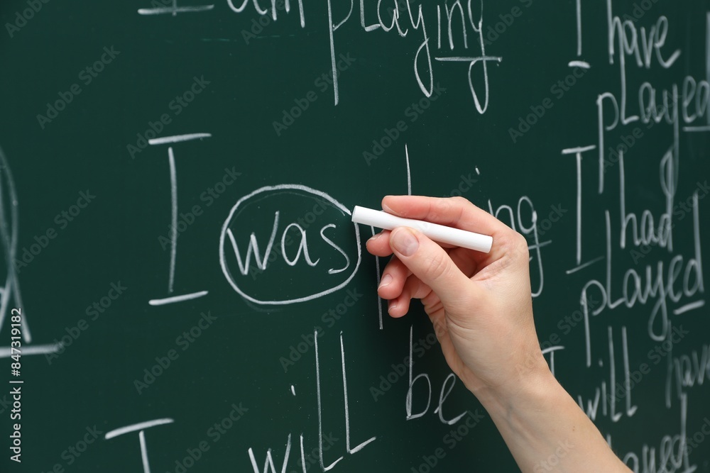 English teacher writing with chalk on green chalkboard, closeup English teacher writing with chalk on green chalkboard, closeup