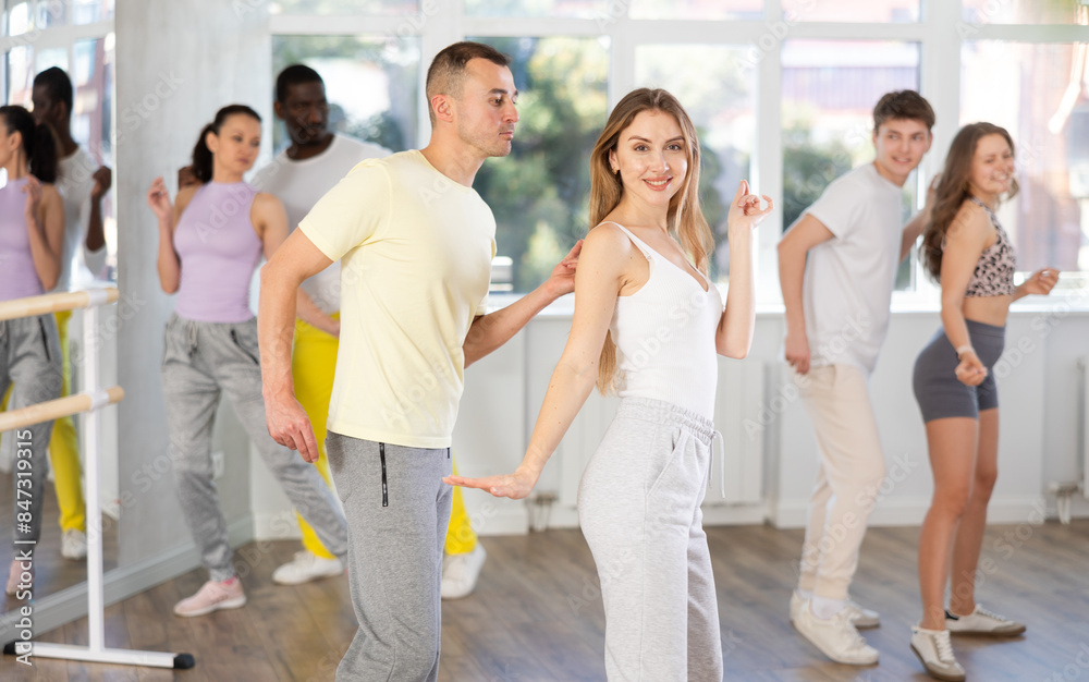 Fototapeta premium Motivated cheerful young adult couple, man and woman in casual sportswear dancing vigorous lindy hop at group dance rehearsal in modern choreography studio..