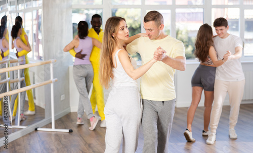 Slim young man and woman practicing waltz dance in training hall during group dancing classes photo