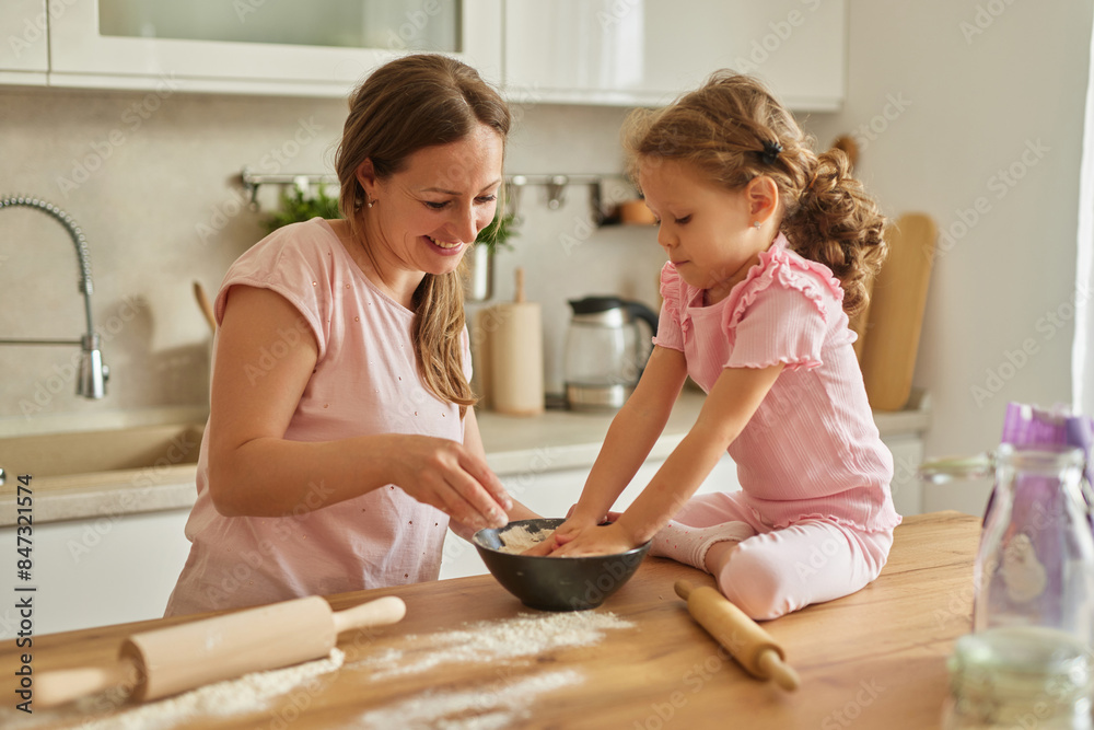Mother and her daughter kneading dough at wooden table in kitchen
