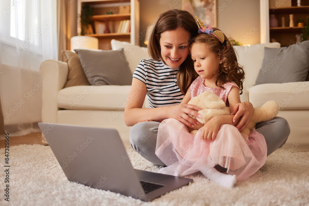 Smiling mother and daughter sitting on carpet and using laptop Smiling mother and daughter sitting on carpet and using laptop