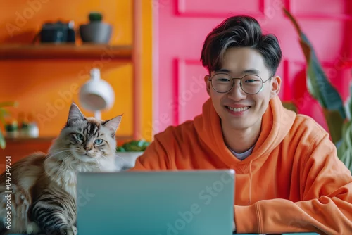 Fototapeta Happy Asian Man Working on Laptop with Cat in Bright and Colorful Home Office