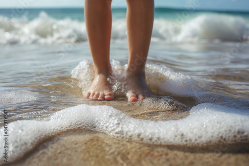 Child's feet on the seashore washed by a wave, close-up photo