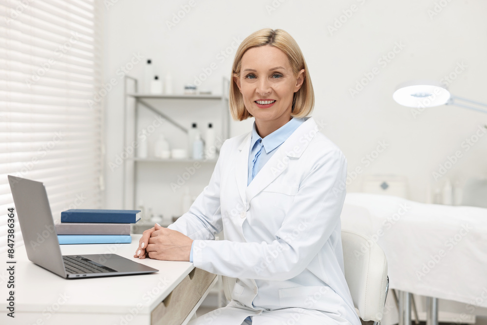 Portrait of happy dermatologist at white table in clinic Portrait of happy dermatologist at white table in clinic