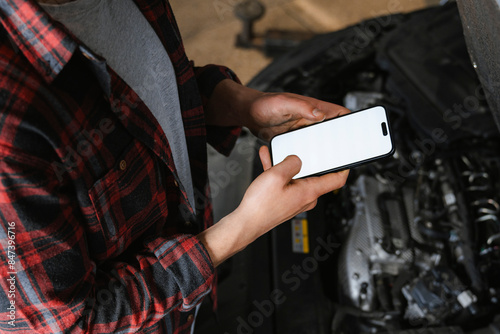 A man uses a mobile phone with white screen in a car repair shop
